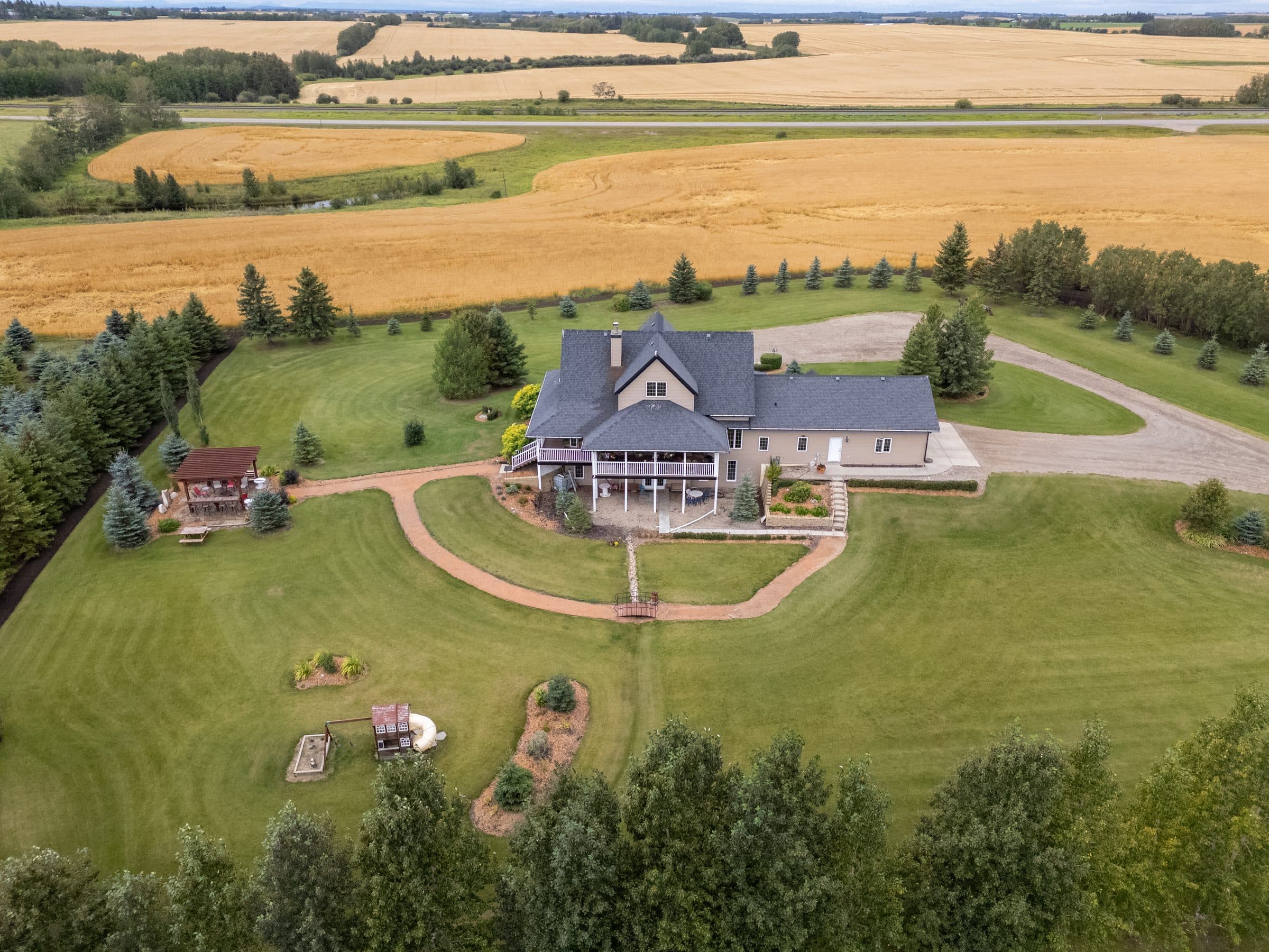 Aerial of an acreage home and lawns with wheat fields beyond