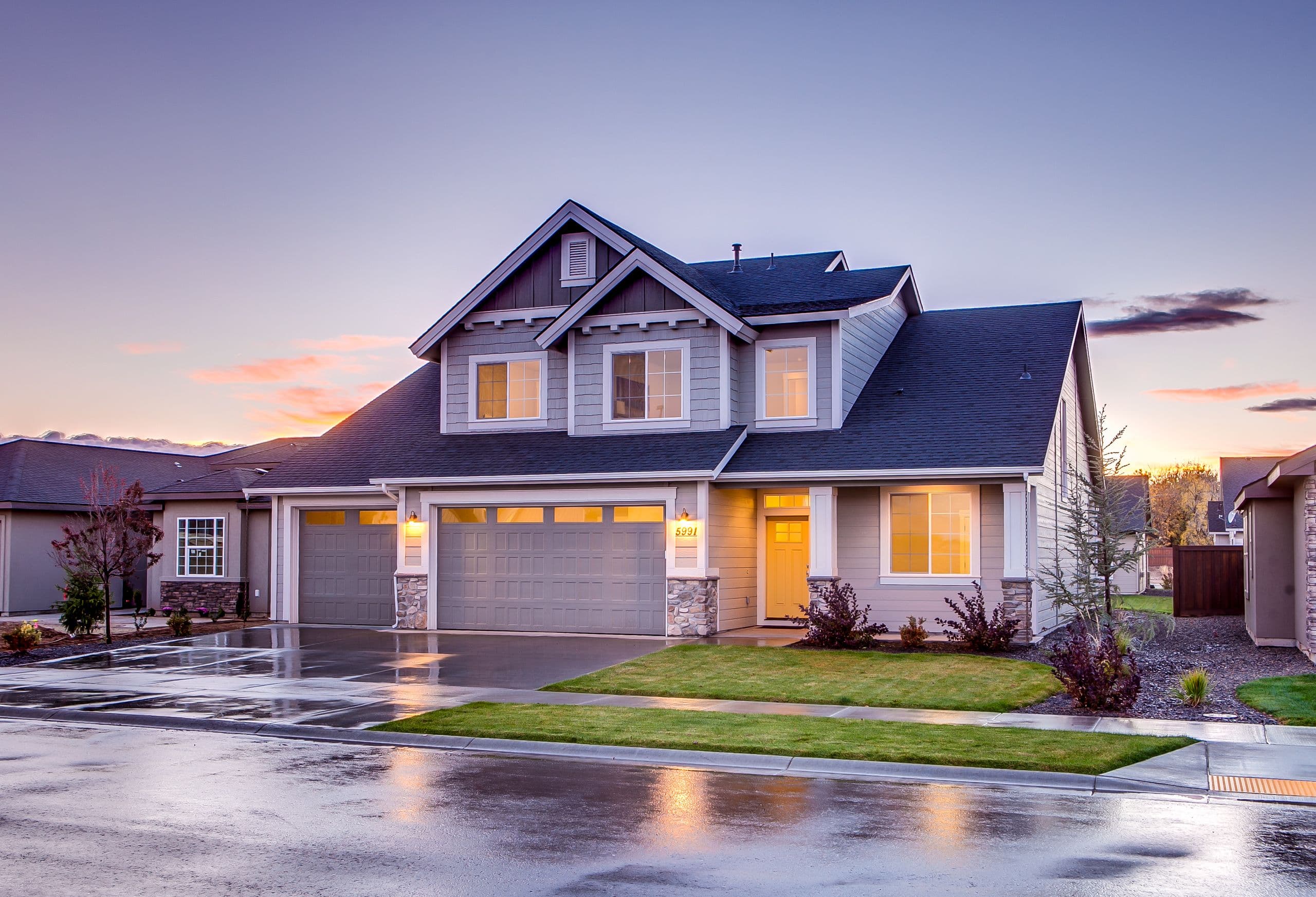 Two-storey craftsman home at twilight with its garage and windows lit and a wet driveway