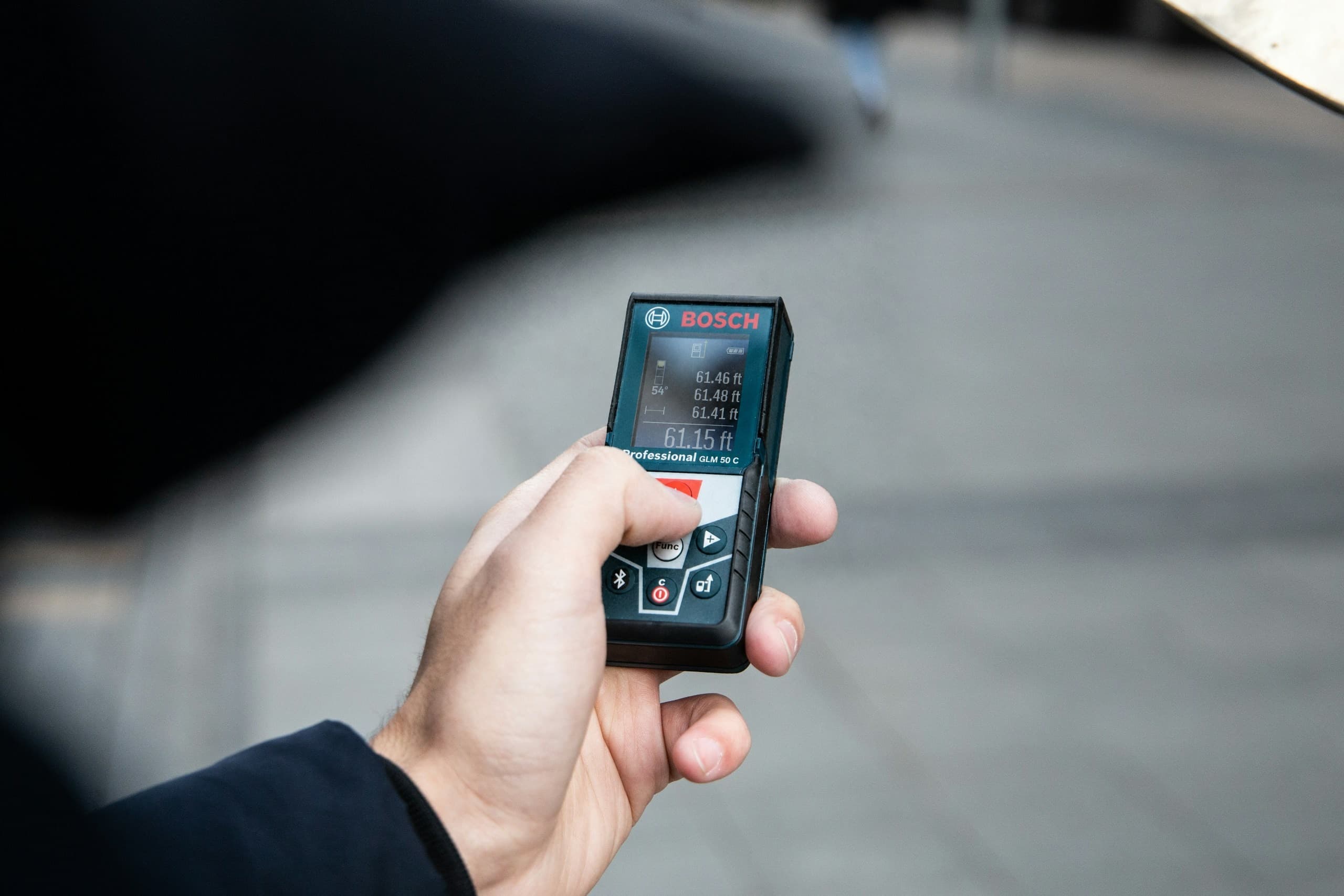 Hand holding a laser distance meter with measurements in feet on its screen